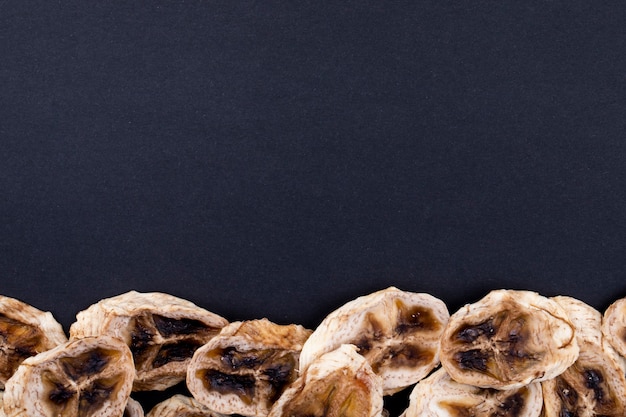 Top view of dried banana chips arranged at the bottom on black background with copy space