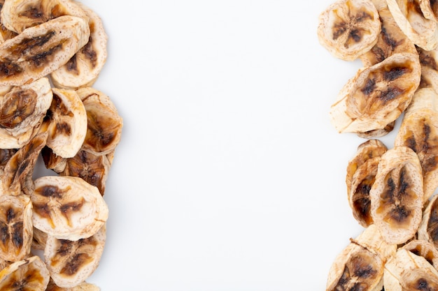 Top view of dried banana chips arranged on sides on white background with copy space