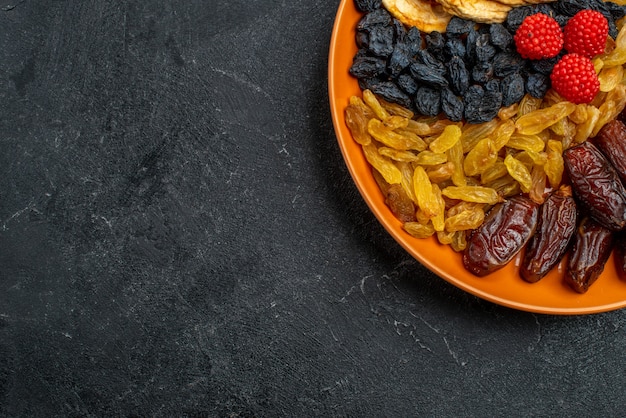 Top view dried fruits with raisins inside plate on dark grey space