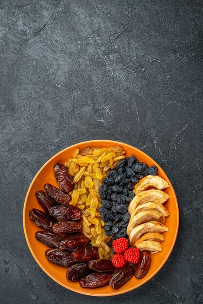 Top view dried fruits with raisins inside plate on grey desk