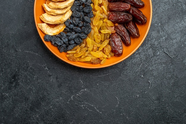 Top view dried fruits with raisins inside plate on grey space