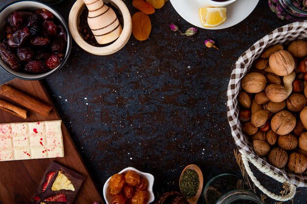 Top view of dried fruits with walnuts, chocolate bars and spices on black with copy space