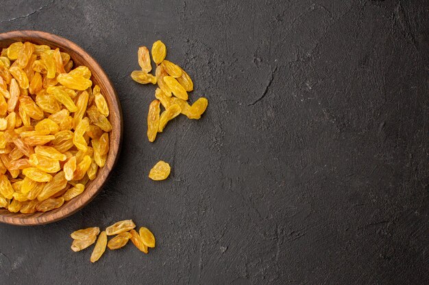 Top view of dried grape raisins inside plate on dark grey surface