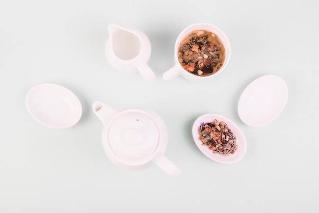 Top view of dried herbs in the tea near crockery on white surface