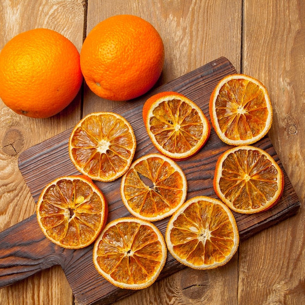 Вид сверху сушеный апельсин на разделочную доску и свежие апельсины на деревянный стол