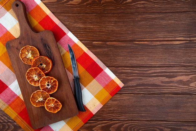 Вид сверху сушеные апельсиновые дольки с кухонным ножом на деревянной разделочной доске на деревянный фон с копией пространства