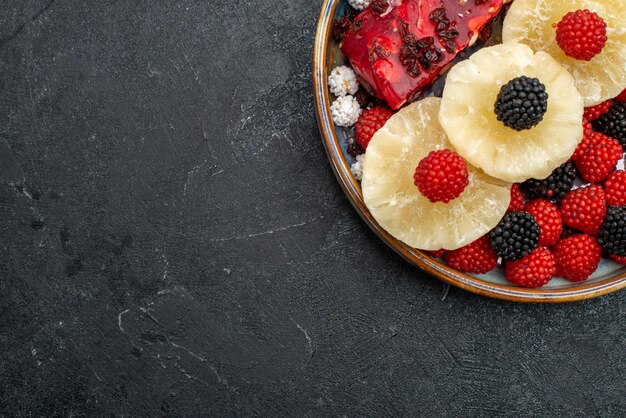 Free photo top view dried pineapple rings with confiture berries on dark-grey surface