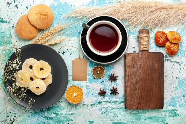 Вид сверху сушеных колец ананаса с чашкой чая и печеньем на синем фоне, торт, выпечка, фруктовый бисквит, сладкое сахарное печенье
