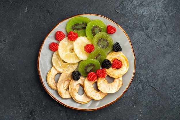 Top view dried pineapple rings with dried kiwis and apples on dark-grey surface