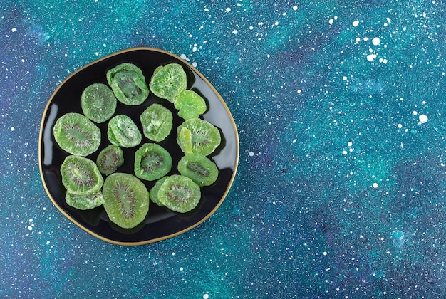 Top view of dry kiwi slices on black plate. 