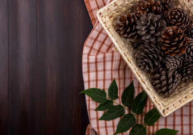 Top view of dry pine cones in a basket with leaf on checked tablecloth and wood