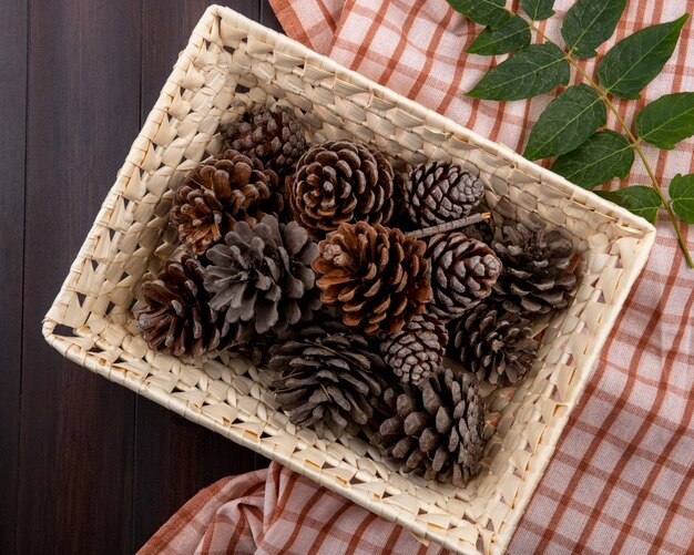 Top view of dry pine cones on basket with leaf on checked tablecloth and wood