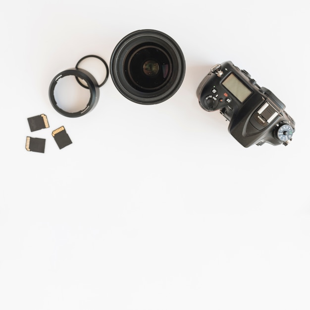 Top view of dslr camera; memory cards and camera lens with extension rings on white backdrop