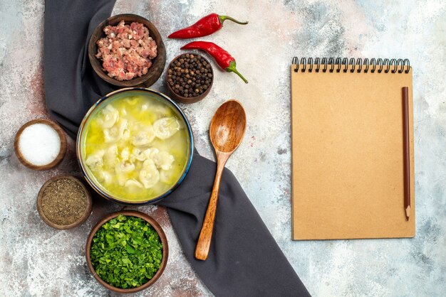 Top view dushbara black tablecloth bowls with meat different spices greens wooden spoon notepad on nude surface