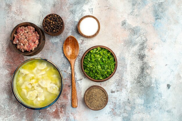 Top view dushbara bowls with different spices greens meat wooden spoon on nude surface free place food photo