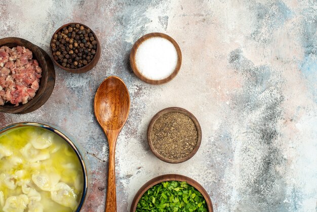 Top view dushbara bowls with different spices greens meat wooden spoon on nude surface free space