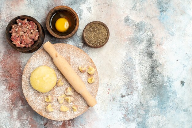 Top view dushbara dough rolling-pin on dough pastry board bowls with meat pepper and egg yolk on nude surface free place