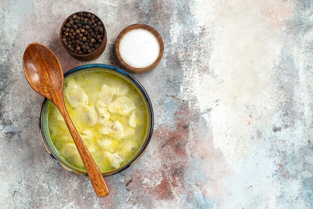 Top view dushbara dumplings soup bowls with salt pepper wooden spoon on bowl on nude surface free place azerbaijani dish