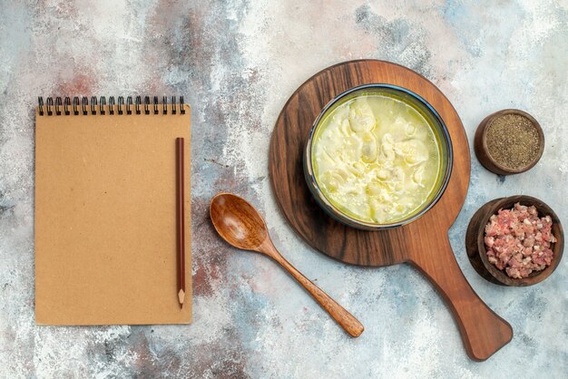 Top view dushbara dumplings soup on cutting board bowls with meat and pepper wooden spoon a notebook on nude surface