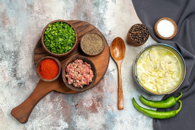 Top view dushbara a wooden spoon black kitchen towel hot pepper bowls with black pepper salt bowls with meat greens different spices on chopping board on nude surface