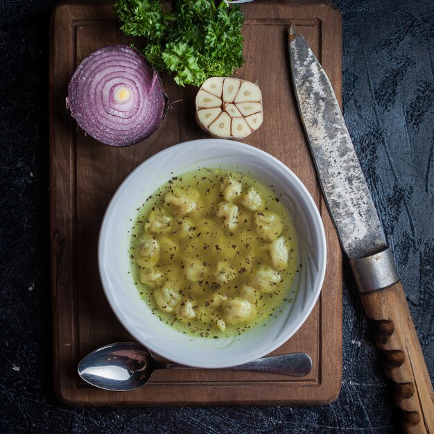 Top view dushpara with knife and spoon and onion and garlic in food board