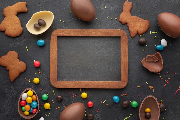 Top view of easter chocolate eggs with bunny shaped cookies and blackboard