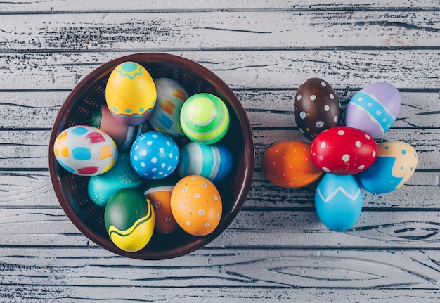 Uova di pasqua di vista superiore in ciotola su fondo di legno leggero.