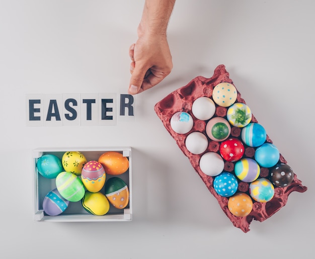 Top view easter eggs in wooden box and egg carton with easter text on white background.