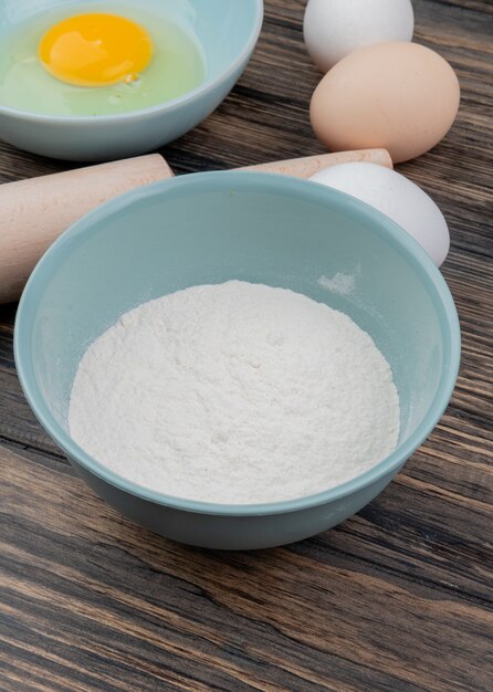 木製の背景に青いボウルに小麦粉と青いボウルに卵黄と卵白のトップビュー