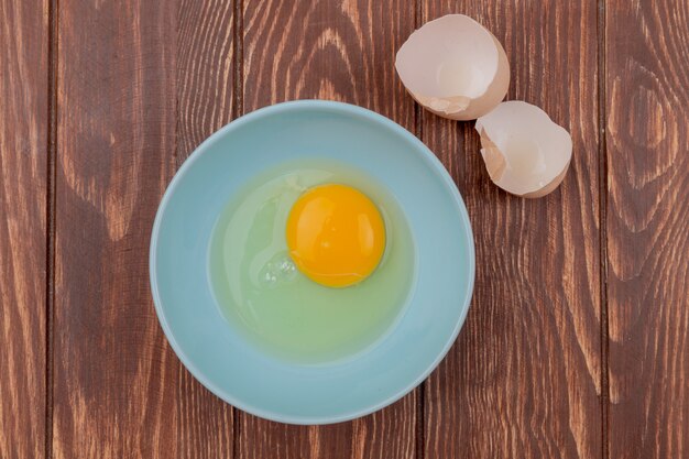 Top view of egg yolk and white on a white bowl with shells of eggs on a wooden background