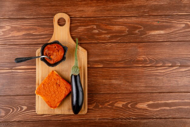 Top view of eggplant caviar in saucer and toast with vegetables caviar fresh ripe eggplant on wooden board on rustic background with copy space