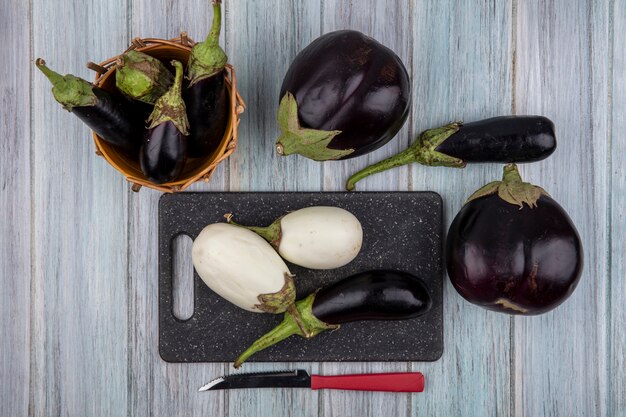 Top view of eggplants on cutting board and in basket with knife on wooden background