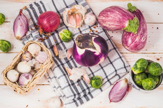 Top view of eggplants; onions; brussels sprouts; garlic cloves and textile on wooden surface