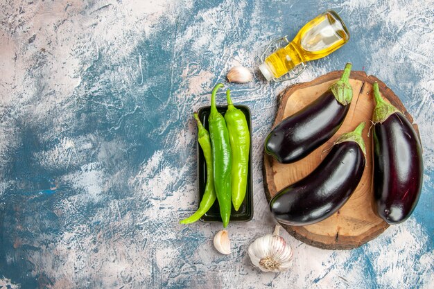 Top view eggplants on tree wood board hot peppers on black plate garlic oil on blue-white background