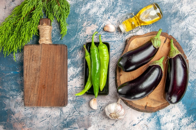 Top view eggplants on tree wood board hot peppers on black plate garlic oil chpping board on blue-white background