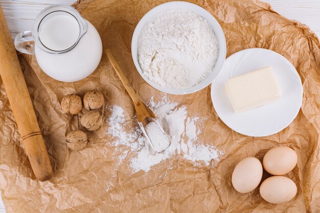 Top view of eggs; cheese; flour; walnuts; rolling pin on brown crumpled paper