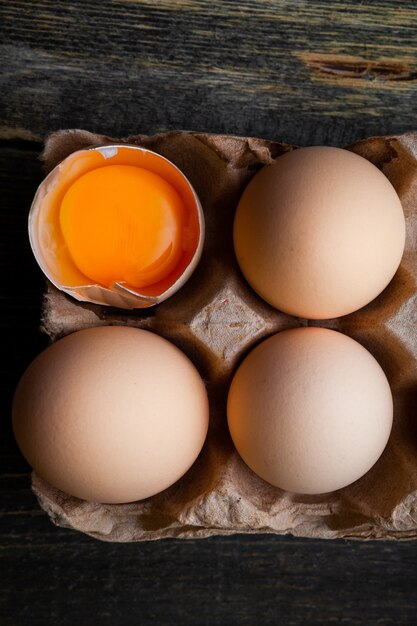 Top view eggs with broken one on dark wooden background. vertical