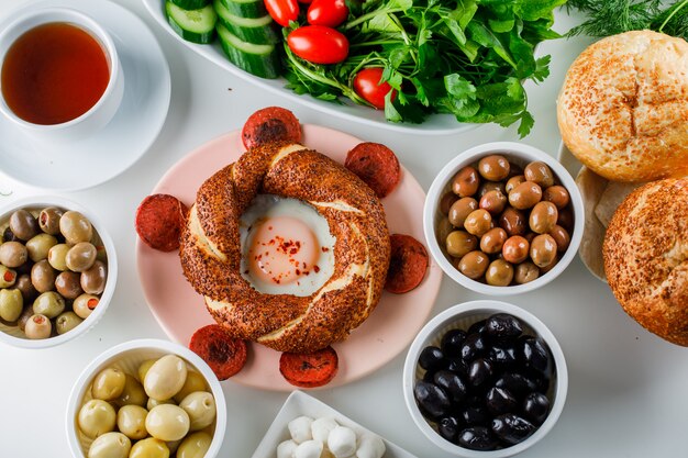 Вид сверху яйца с колбасой в тарелке с чашкой чая, турецкий бублик, салат на белой поверхности
