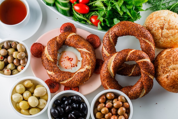 Vista dall'alto uova con salsiccia nel piatto con una tazza di tè, bagel turco, insalata sulla superficie bianca