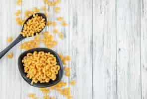 Free photo top view elbow macaroni pasta on the left with copy space on white wooden background