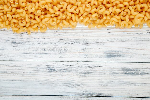 Top view elbow macaroni pasta on top with copy space on white wooden background