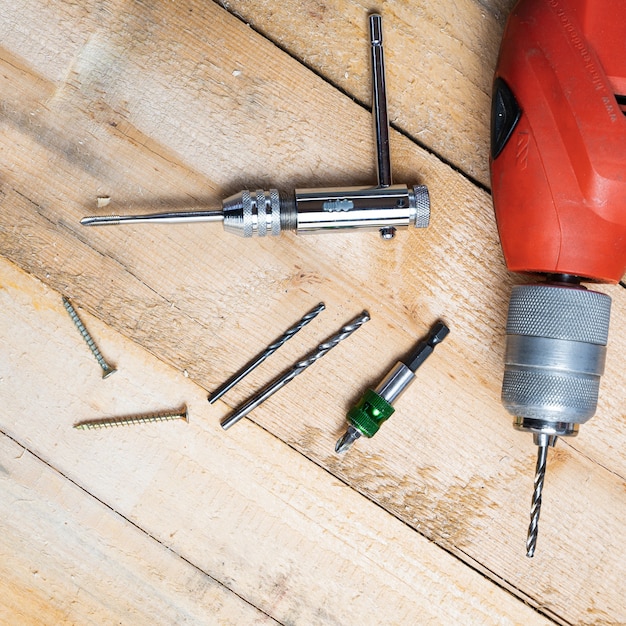 Top view of an electric drill, nails and other repairing equipments on a wooden surface