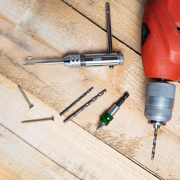 Top view of an electric drill, nails and other repairing equipments on a wooden surface