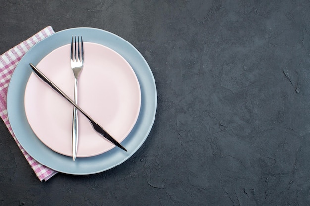 Вид сверху элегантной розовой тарелки с синей тарелкой, ножом и вилкой на темной поверхности