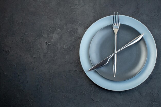 Вид сверху элегантные тарелки с ножом и вилкой на темной поверхности