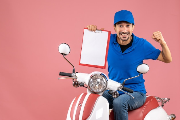 Top view of emotional courier man wearing hat sitting on scooter showing document on pastel peach background