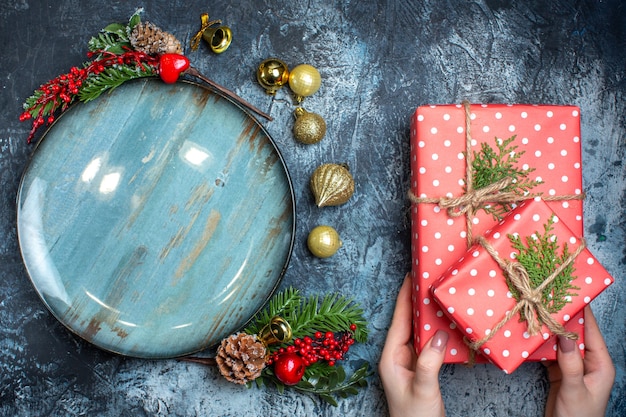 Top view of empty blue plate decorative accessories and hand holding gift boxes on dark background