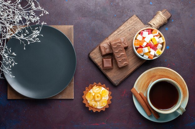 어두운 표면에 차와 사탕으로 형성된 둥근 빈 어두운 접시의 평면도