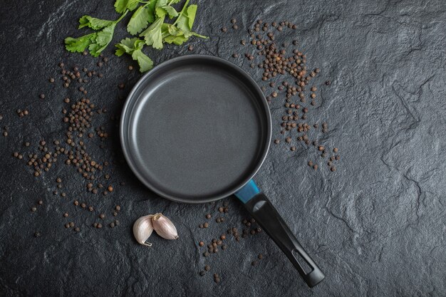 Top view of empty frying pan over black background with garlic and peppers. 