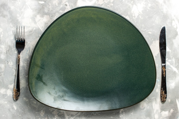 Вид сверху пустая зеленая тарелка, изолированная с вилкой и ножом на светло-сером столе.